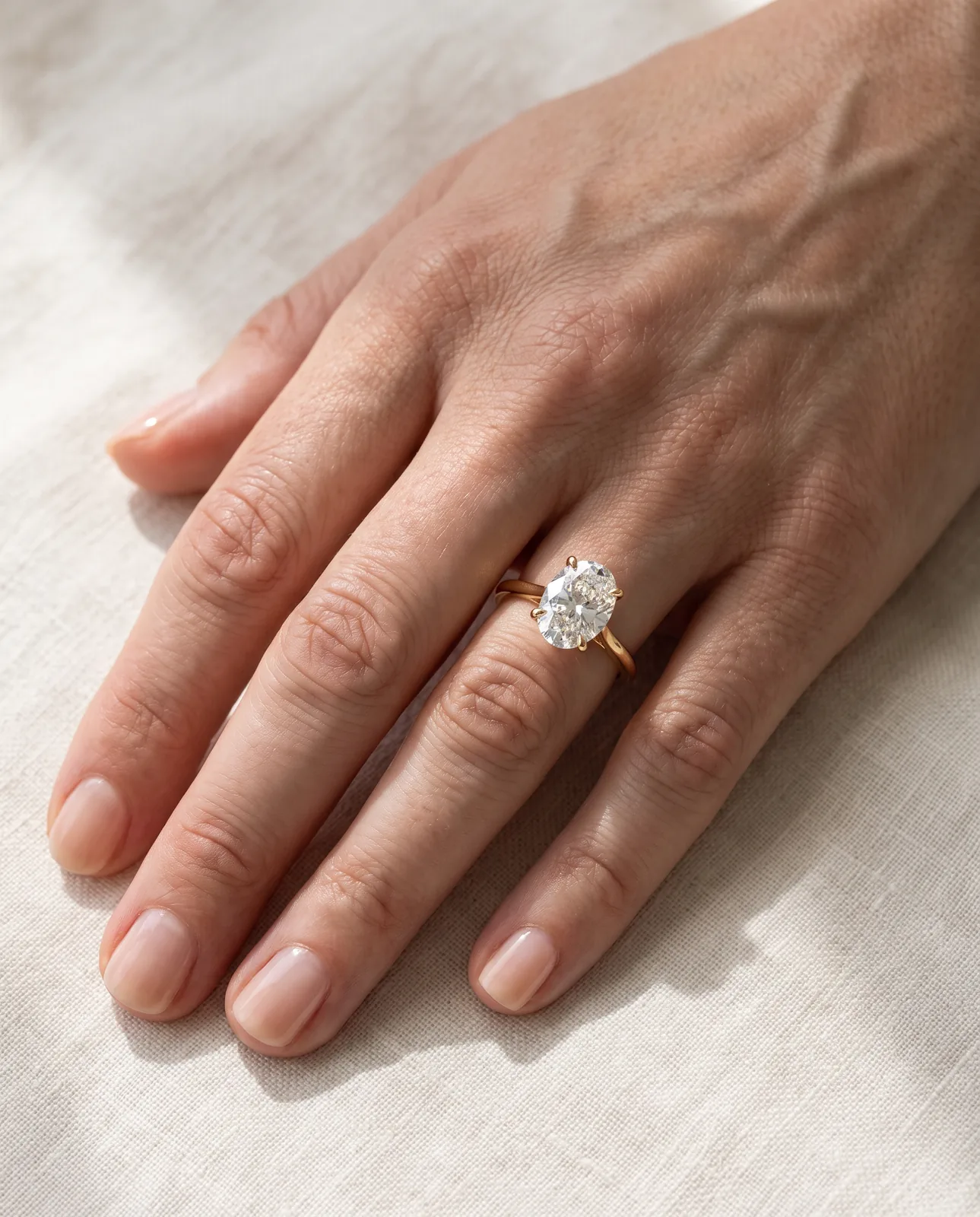 Nano Banana Pro output: the same oval solitaire ring on an adult woman's hand resting on cream linen