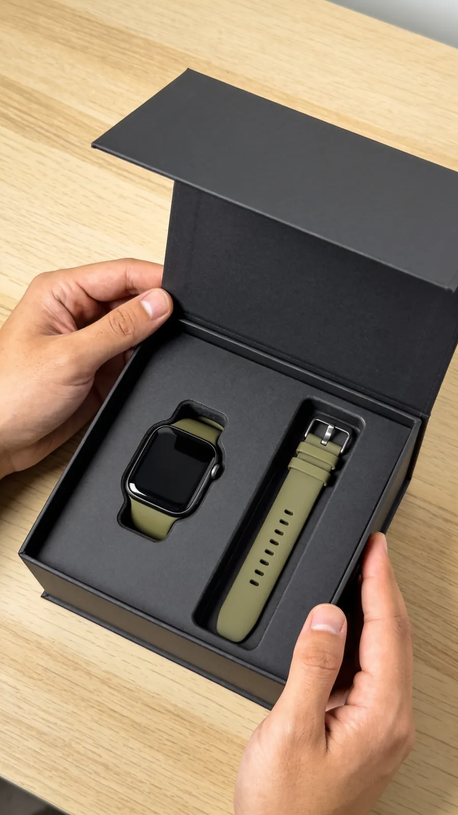 Start frame: top-down view of two hands opening a matte black gift box with a smartwatch and olive green strap inside